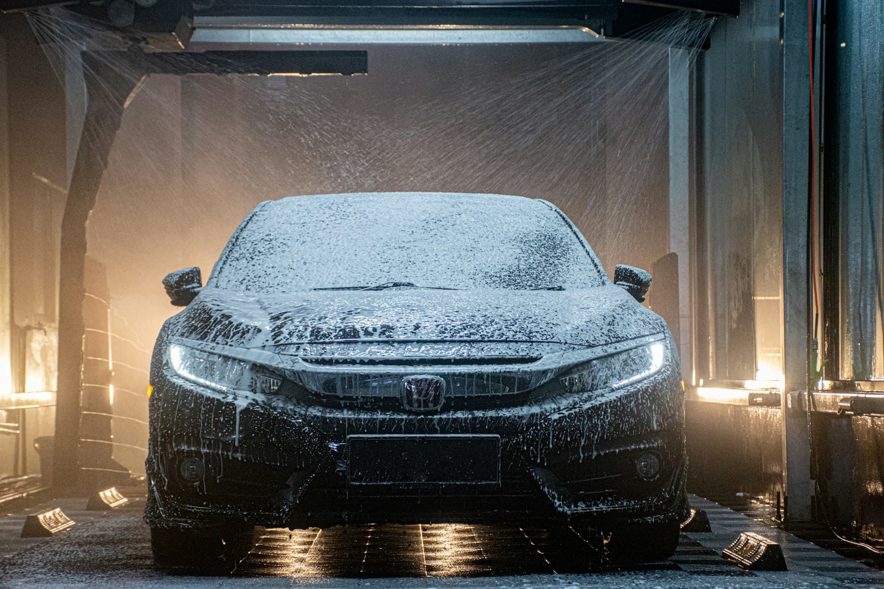 A car covered in foam under the lights of a wash bay