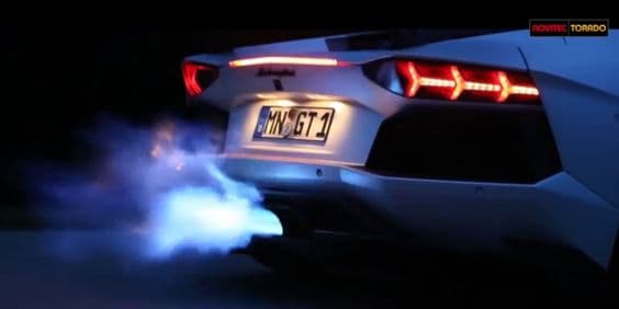 Blue flames from the exhaust of a white sports car at night