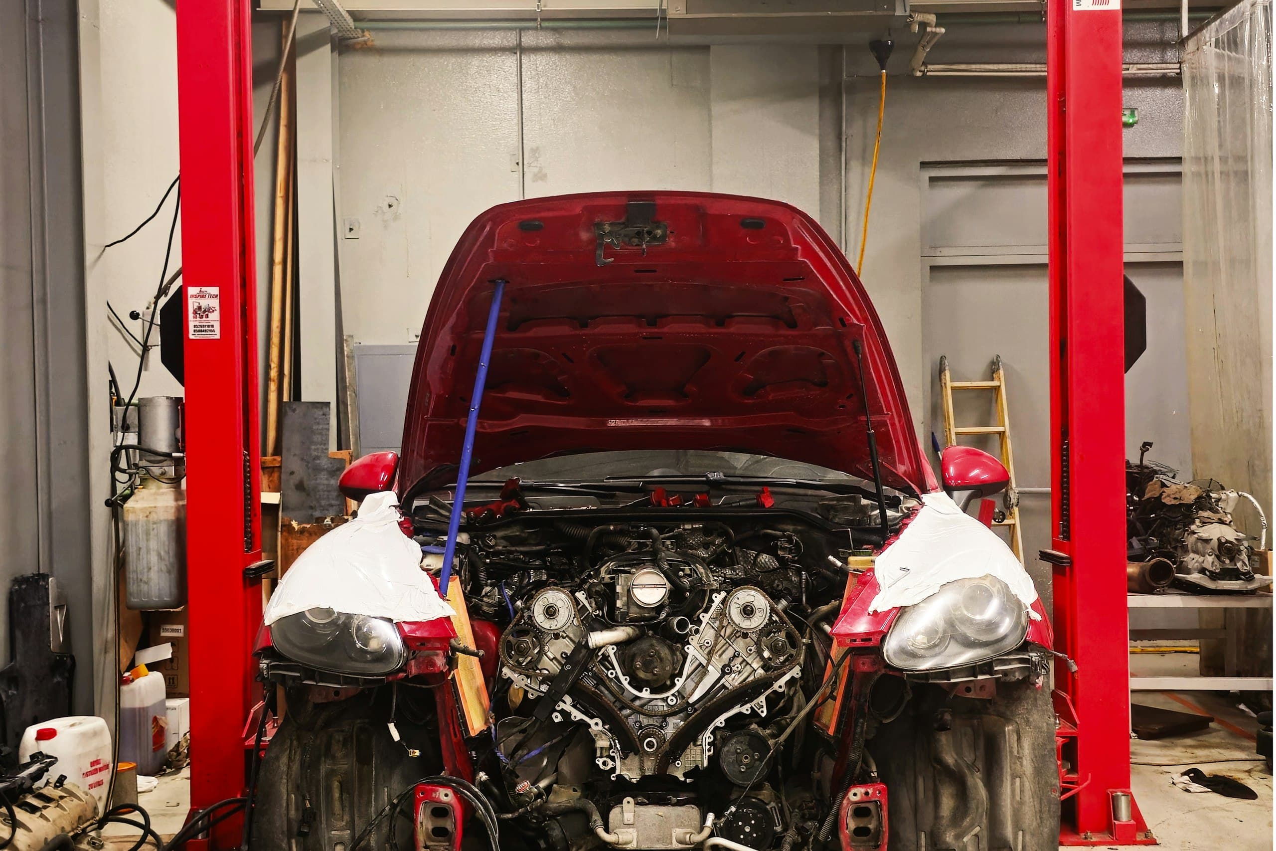 A red car on a two-post lift with its bonnet open