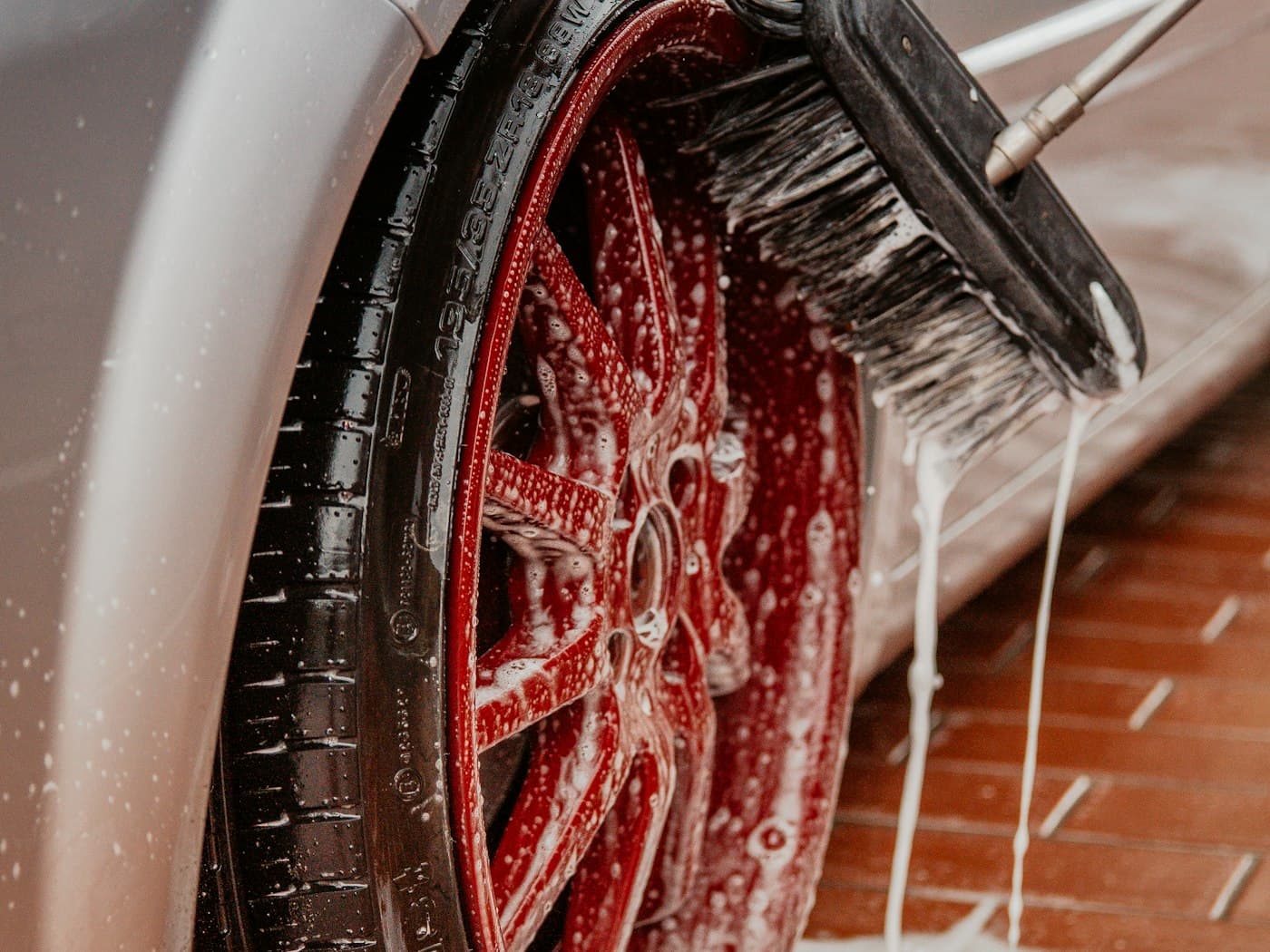 A red alloy wheel being cleaned with a brush